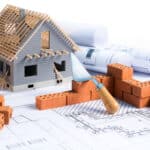 House under construction with bricks, blueprints, and tools on a white background.